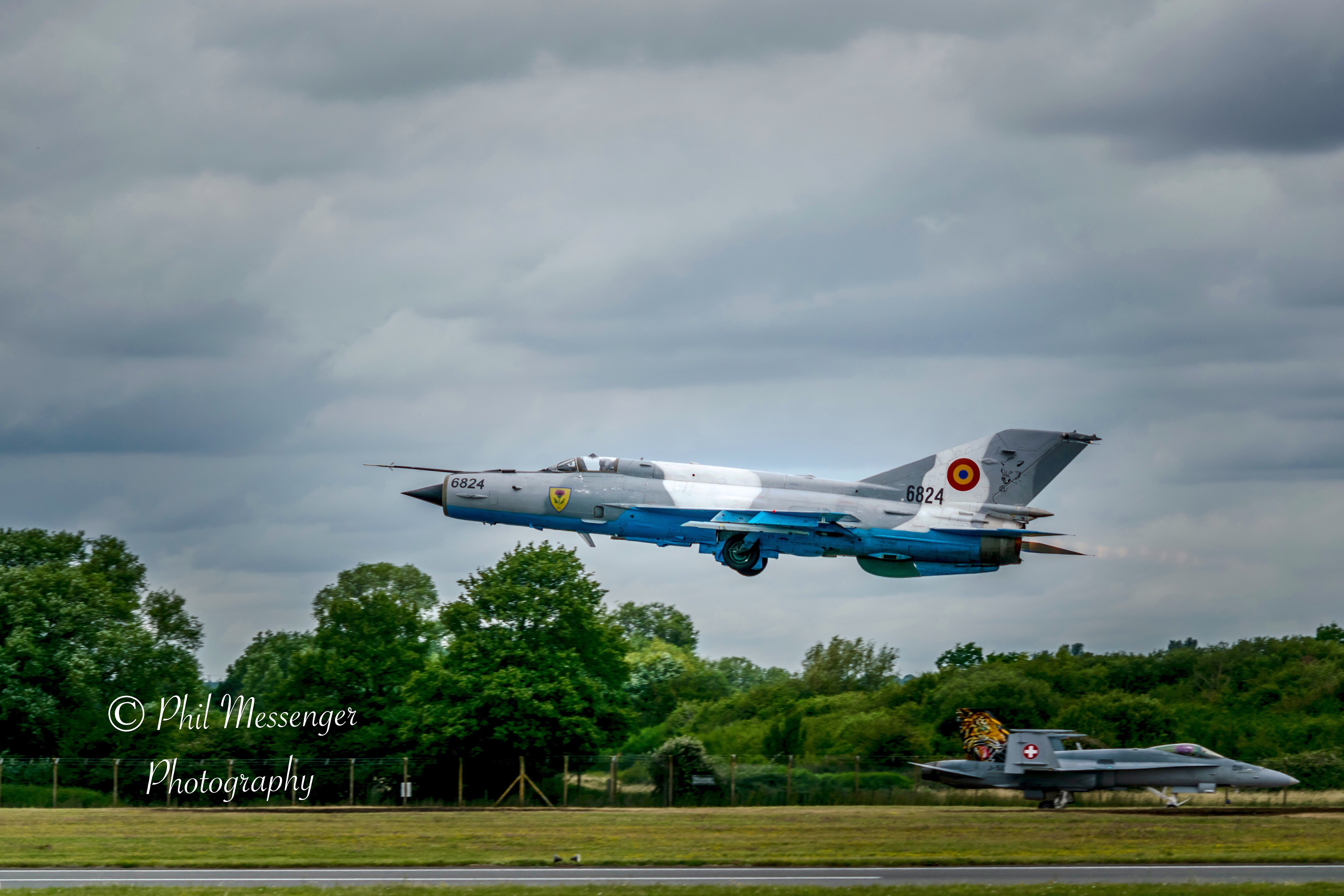 Romanian Air Force MIG-21 Lancer C take off with the Swiss Hornet in the background at The Royal International Air Tattoo.