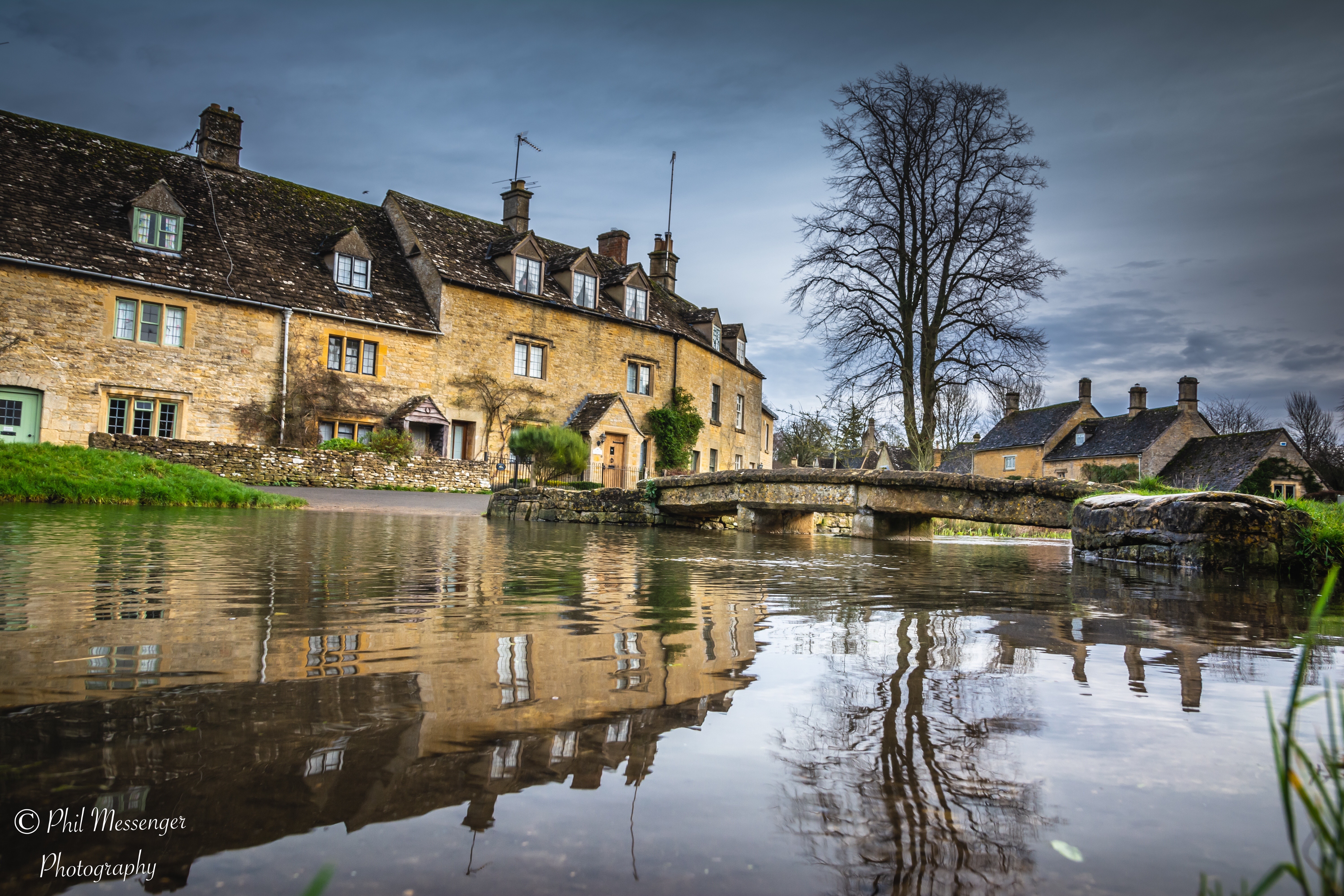 Riverside cottages reflecting on the river eye at Lower Slaughter in the Cotswolds.