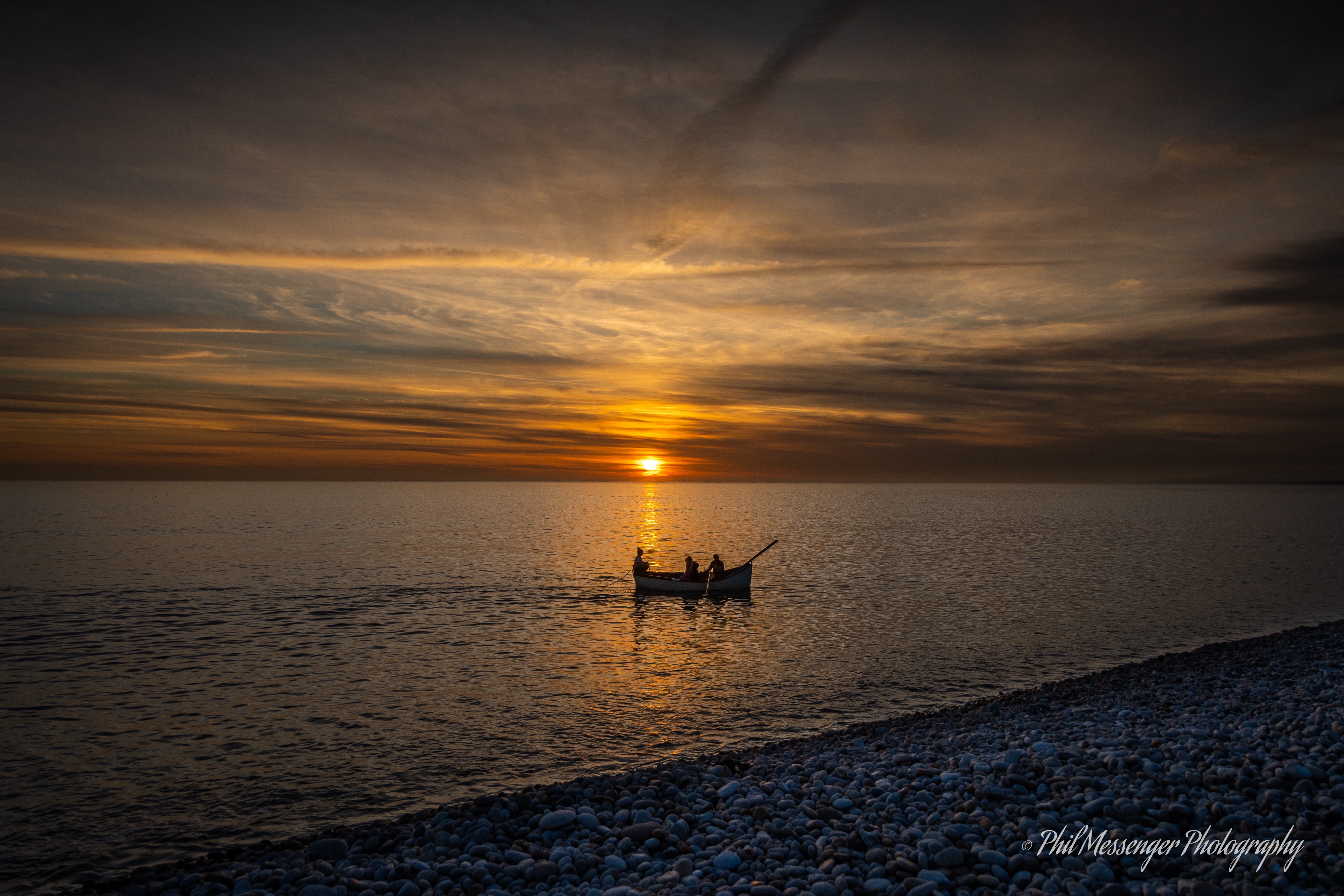 A small fishing boat heading out at sunset on Chesil Beach Portland.